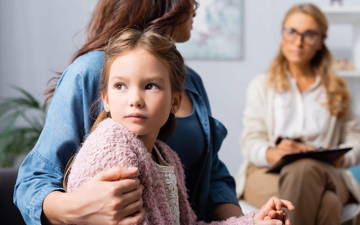 cropped view of mother hugging daughter while visiting psychologist